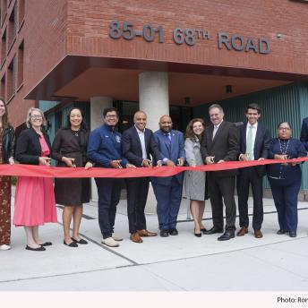 Group photo of people standing in front of a building to cut a ribbon commemorating the opening of  Woodhaven ELLA affordable housing 